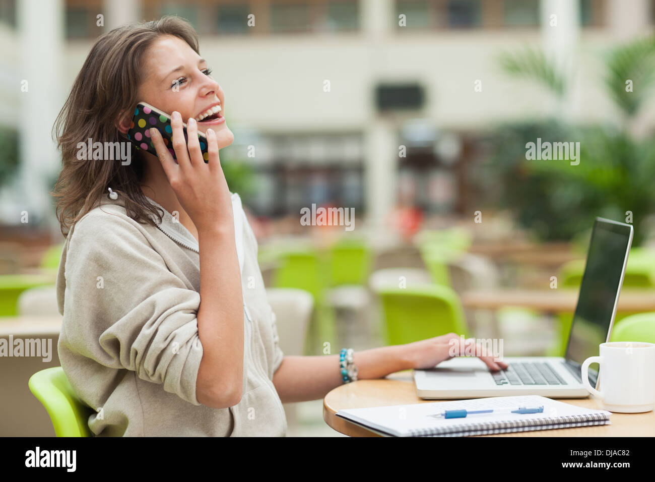 Cheerful student using cellphone and laptop at cafeteria table Stock Photo