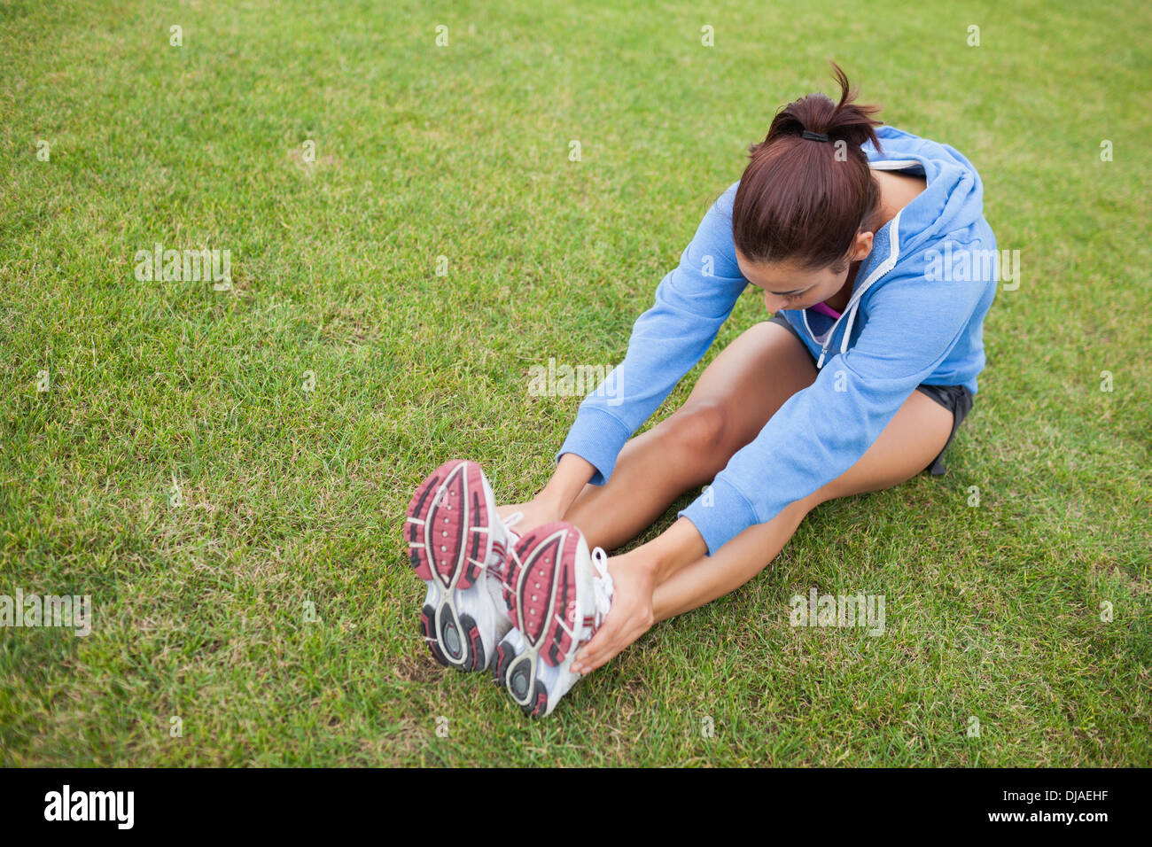 Sporty woman stretching her legs while sitting on the grass Stock Photo ...