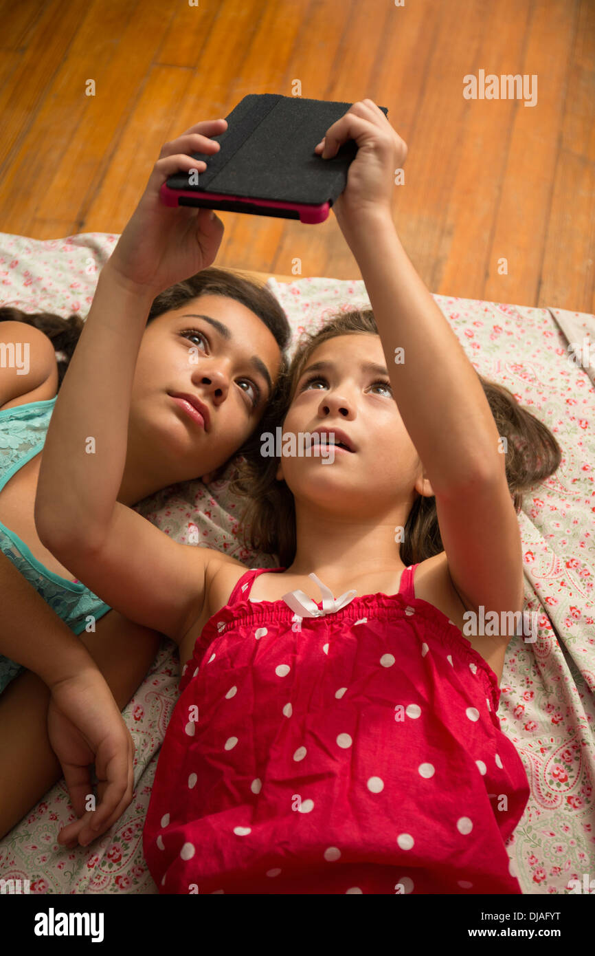 Mixed race sisters using digital tablet on bed Stock Photo