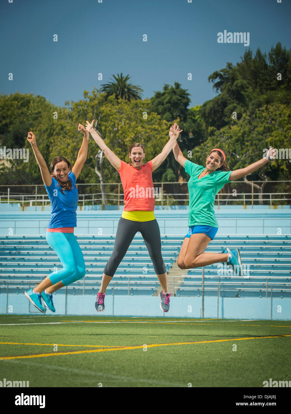 Caucasian women jumping for joy in stadium field Stock Photo