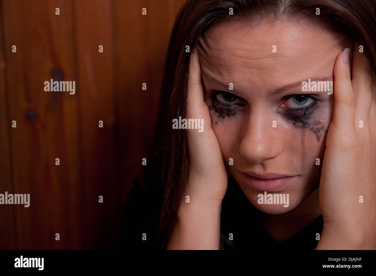 Young woman with her head in her hands and her make-up is running from crying. Stock Photo