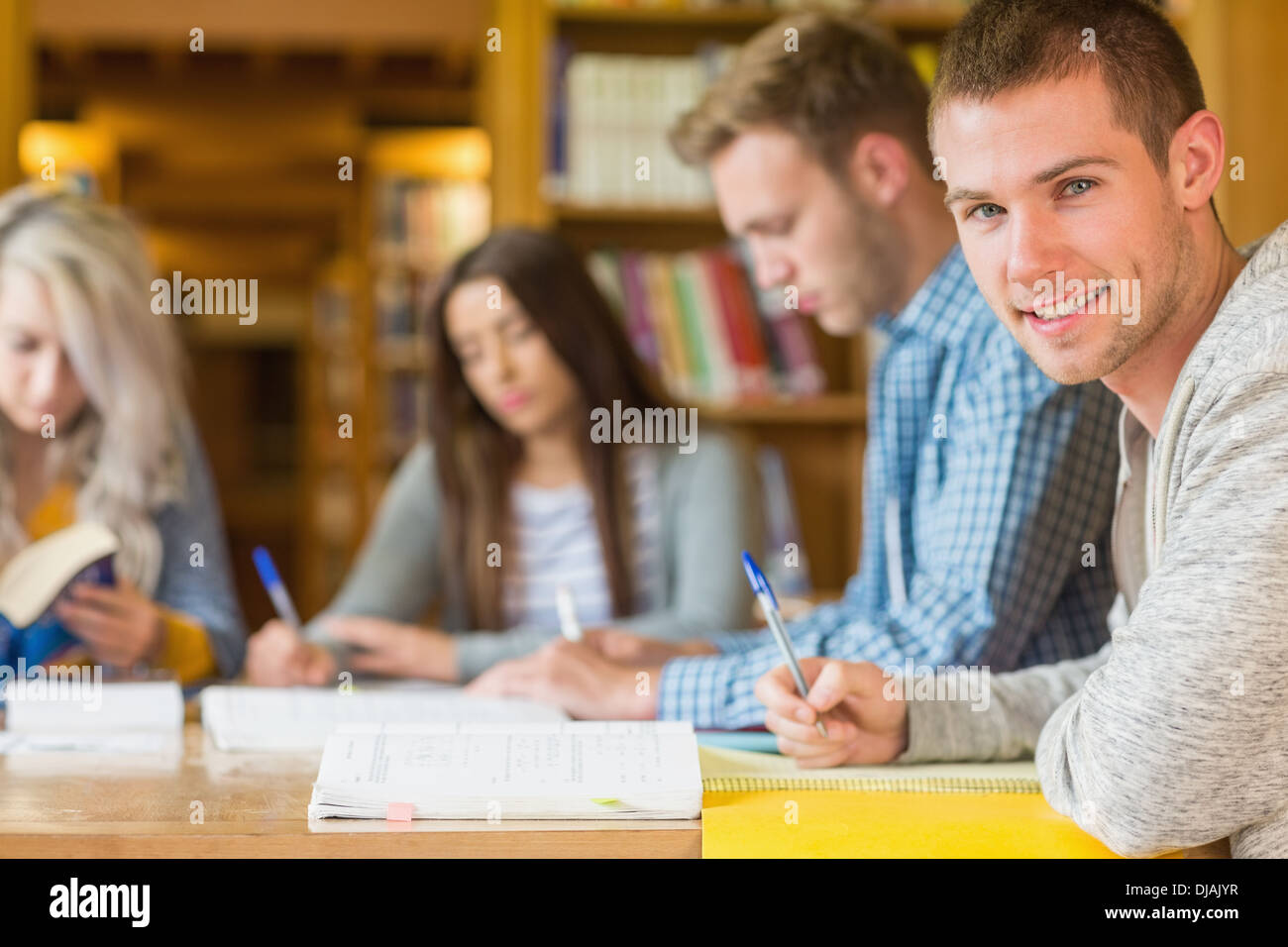 Smiling male student with friends at library desk Stock Photo - Alamy