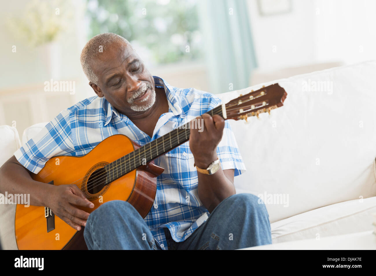 Black man playing guitar on sofa Stock Photo