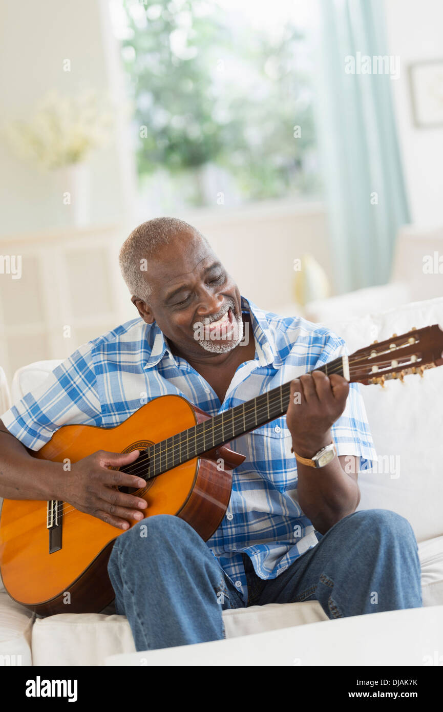 Black man playing guitar on sofa Stock Photo