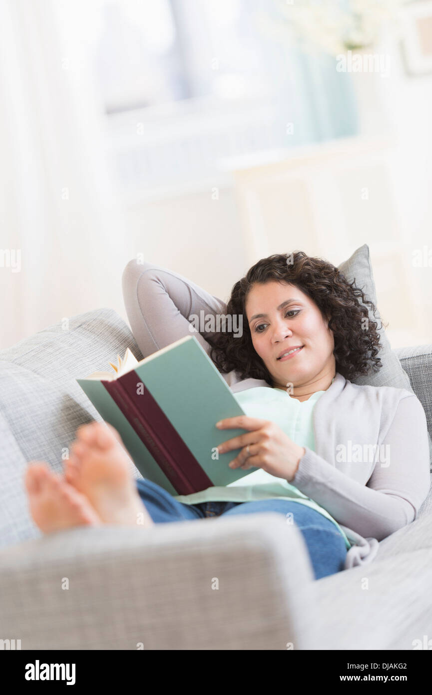 Hispanic woman reading on sofa Stock Photo
