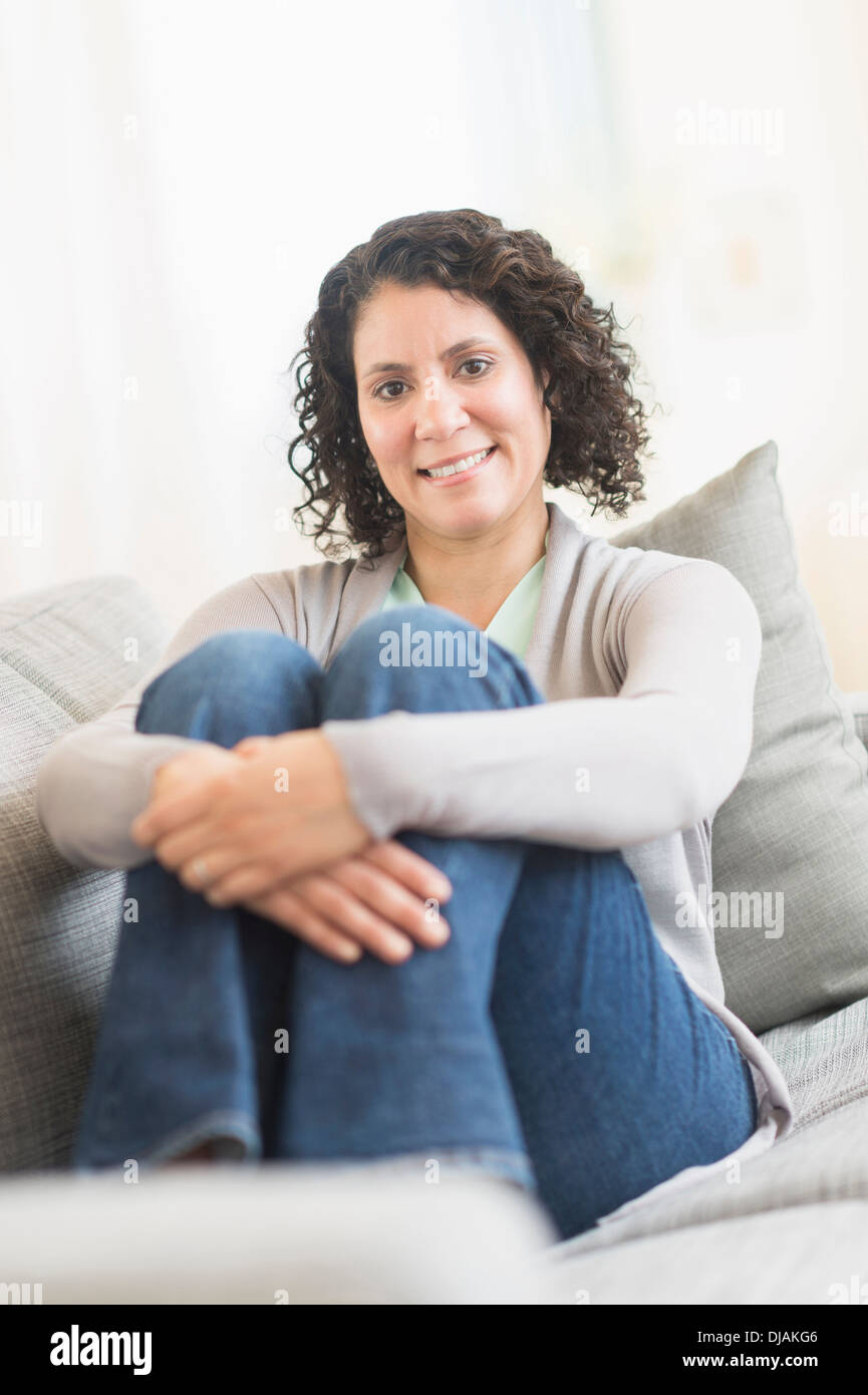 Hispanic woman hugging her knees on sofa Stock Photo - Alamy