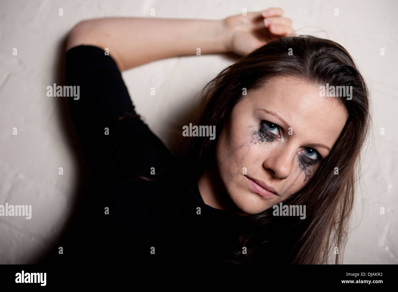 Tearful young woman against a white wall, with her make up running from crying. Stock Photo