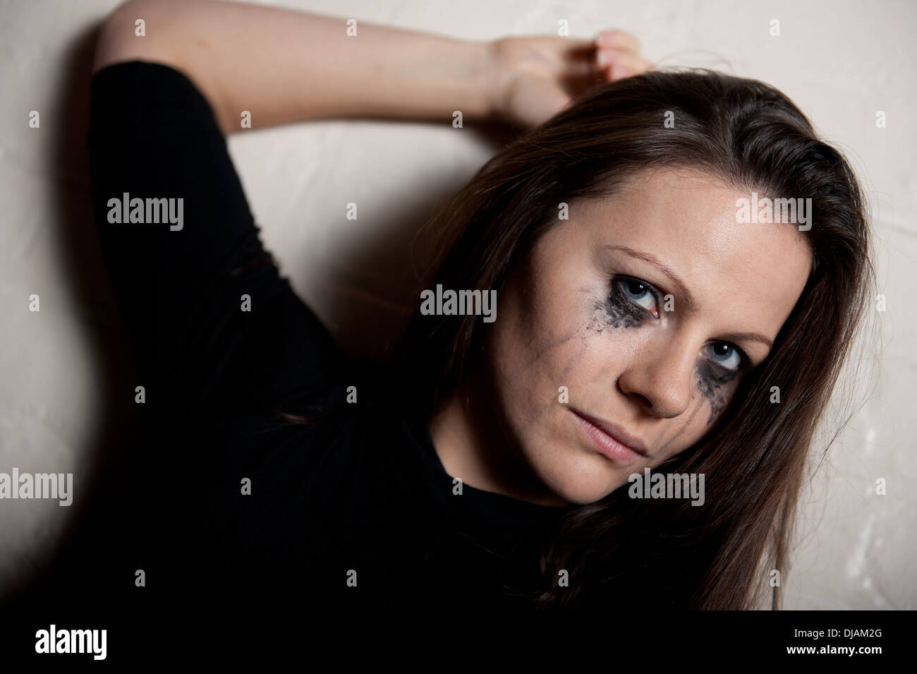 Tearful young woman against a white wall, with her make up running from crying. Stock Photo