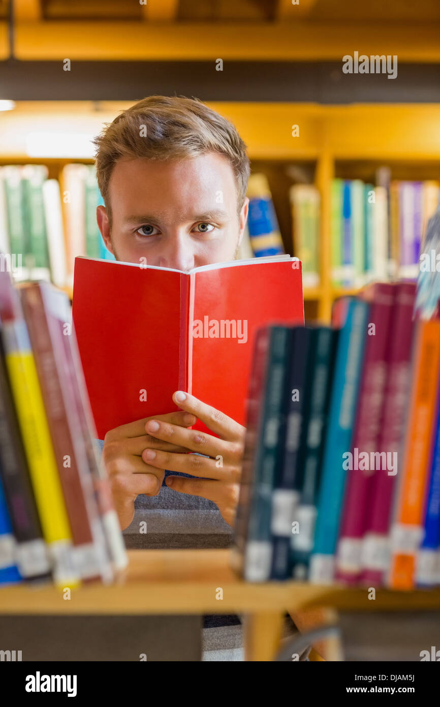 Male student holding book in front of his face in the library Stock Photo