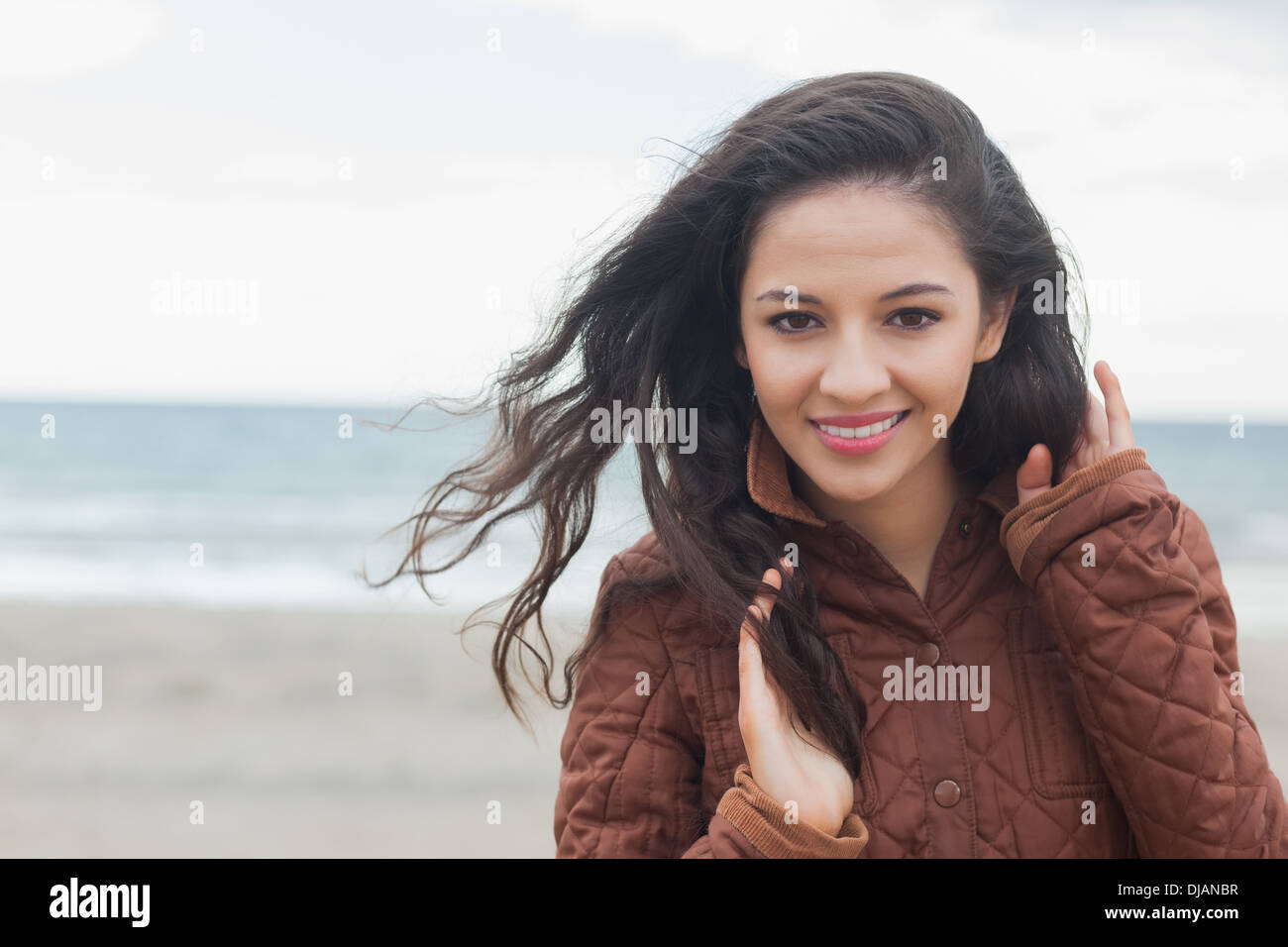 Cute smiling woman in stylish brown jacket on beach Stock Photo