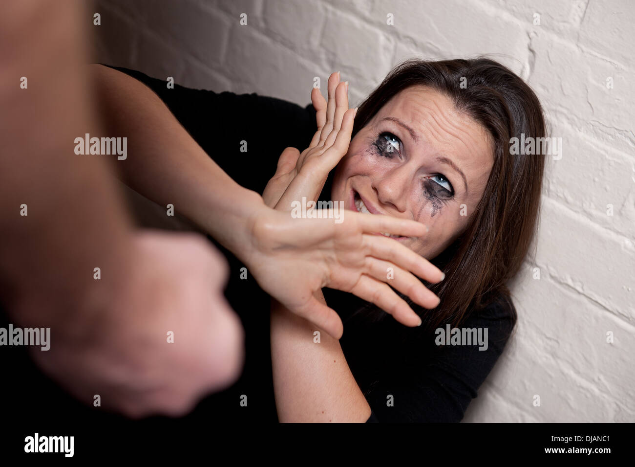 Domestic Violence -Young woman against a white wall trying to protect herself from a man's clenched fist. Stock Photo