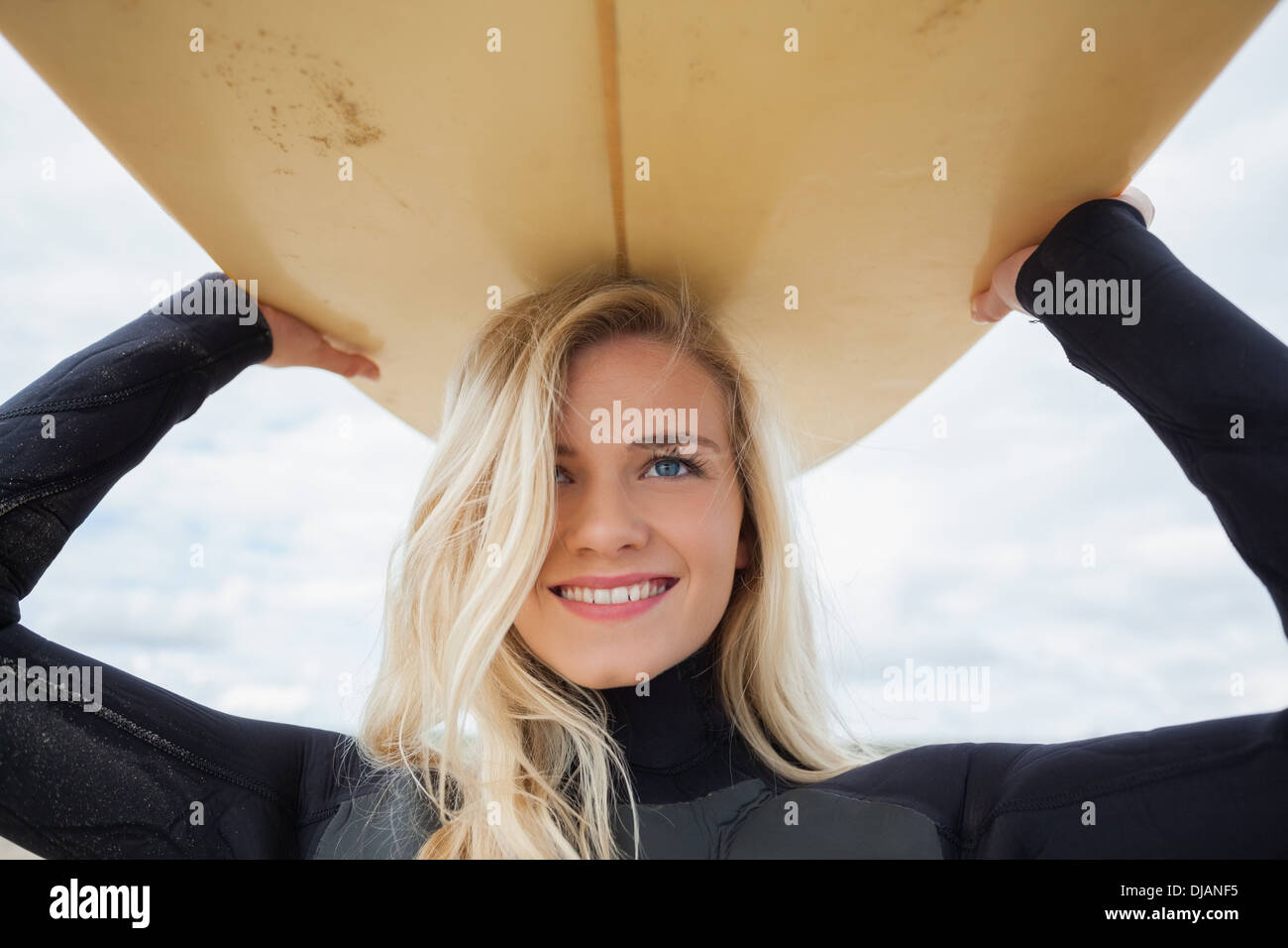 Smiling woman in wet suit holding surfboard over head Stock Photo