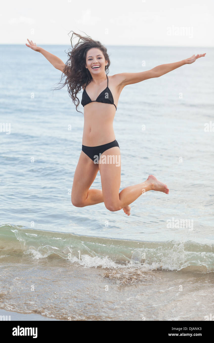 Cheerful young woman in bikini jumping at beach Stock Photo
