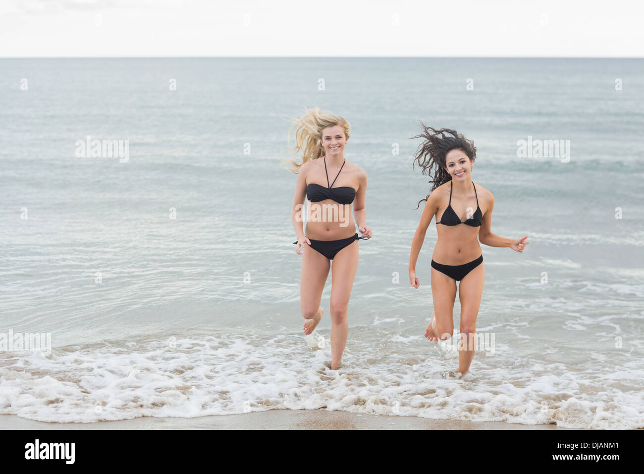 Smiling bikini women running in water at beach Stock Photo