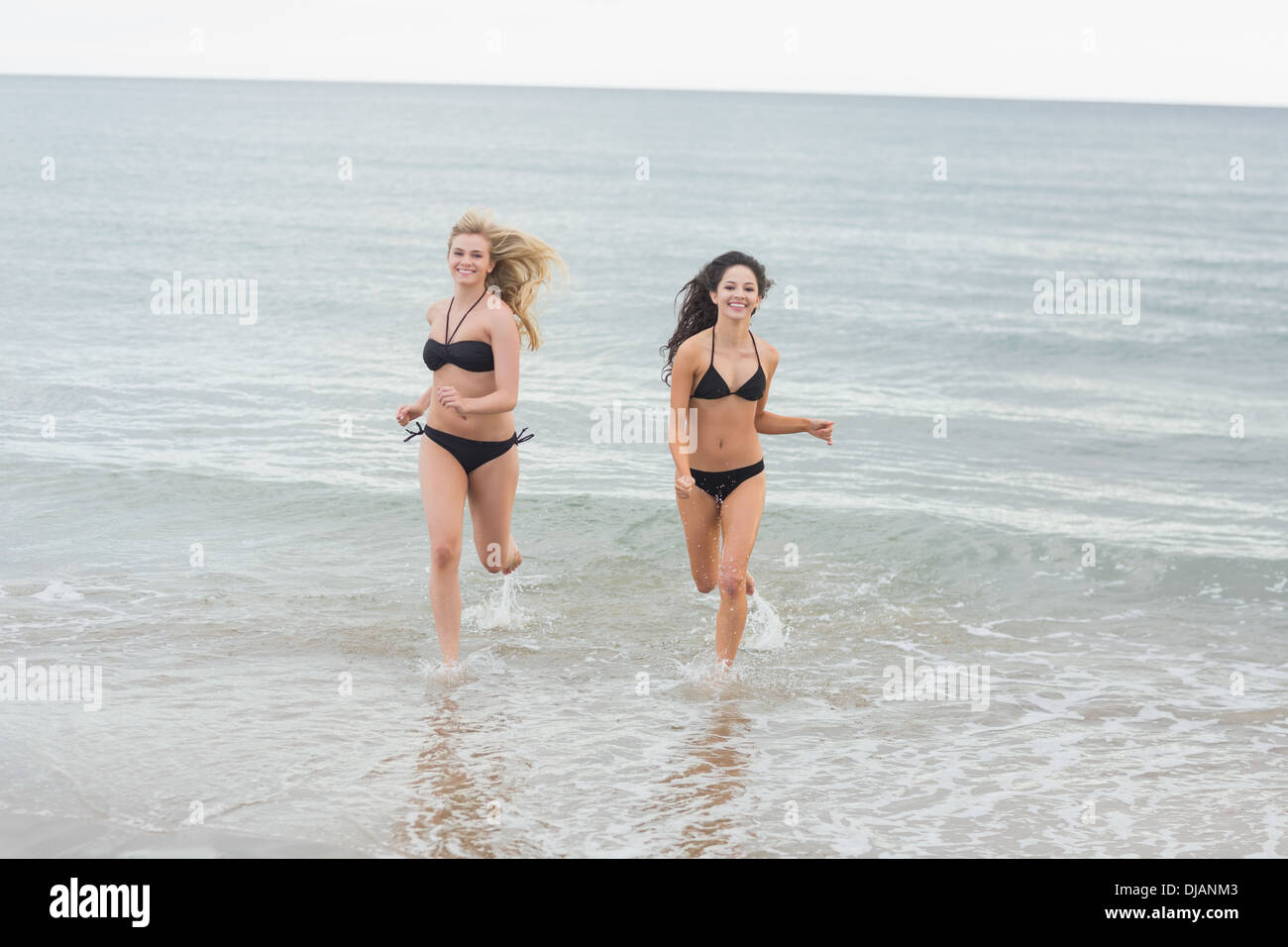 Smiling bikini women running in water at beach Stock Photo