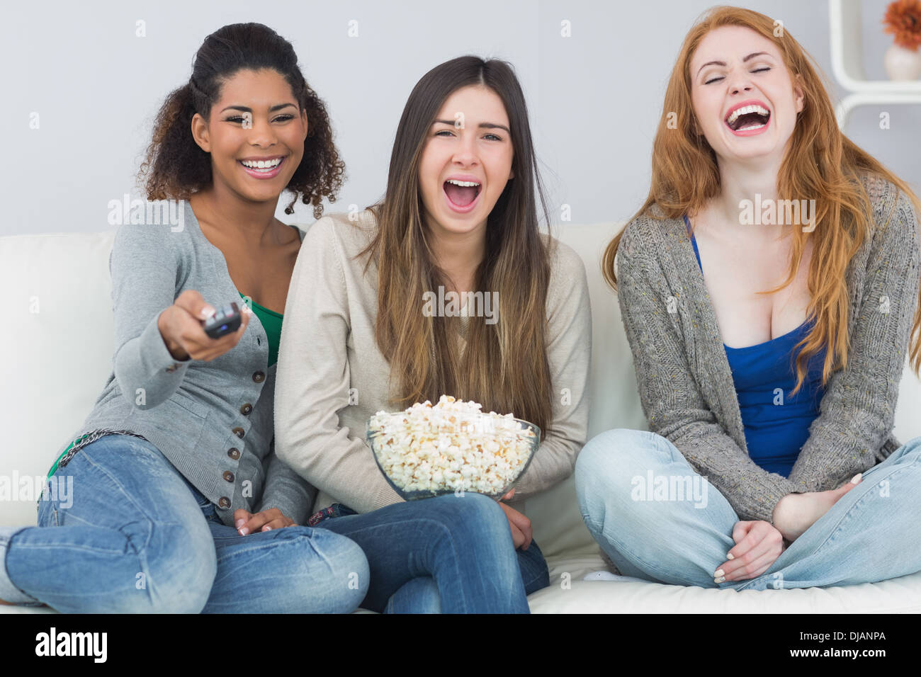 Cheerful friends with remote control and popcorn bowl on sofa Stock Photo