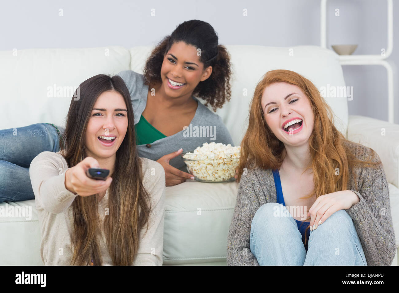 Cheerful friends with remote control and popcorn bowl at home Stock Photo