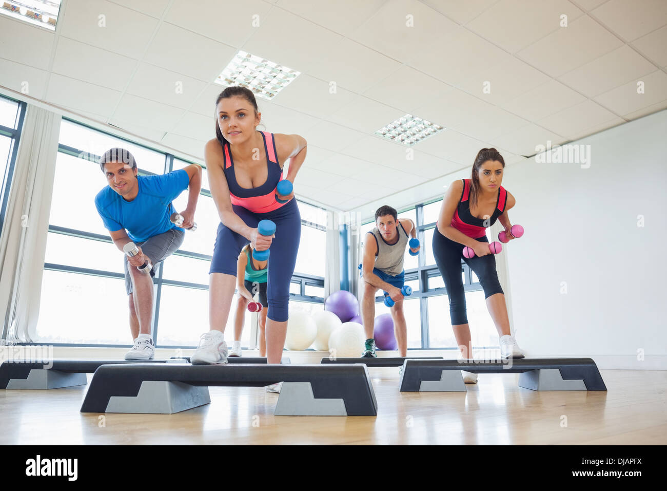 Instructor with fitness class performing step aerobics exercise with ...
