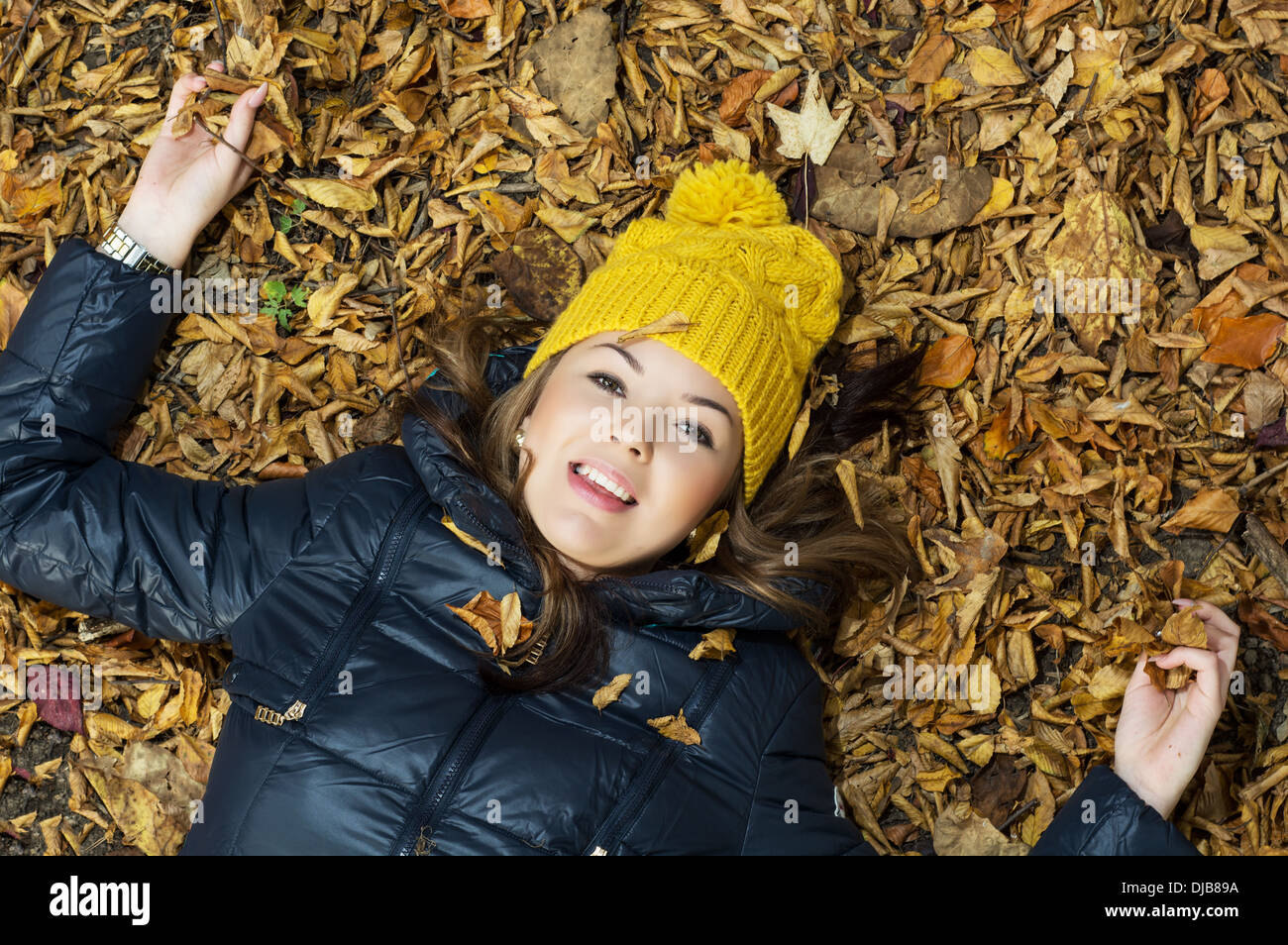 Young smiling teenage girl with yellow cap lying in the autumn leaves ...