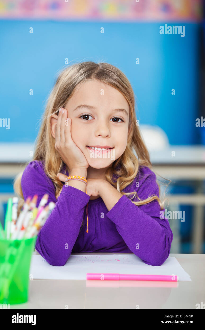 Cute Girl Sitting With Hand On Chin At Desk Stock Photo - Alamy