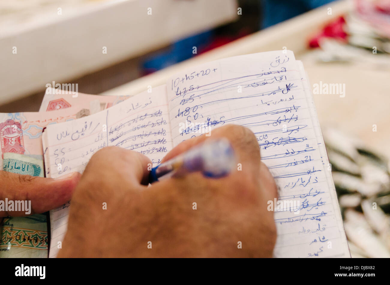 Vendor scribbles some notes on his notebook to record transactions at Deira Fish Market. Dubai, United Arab Emirates. Stock Photo