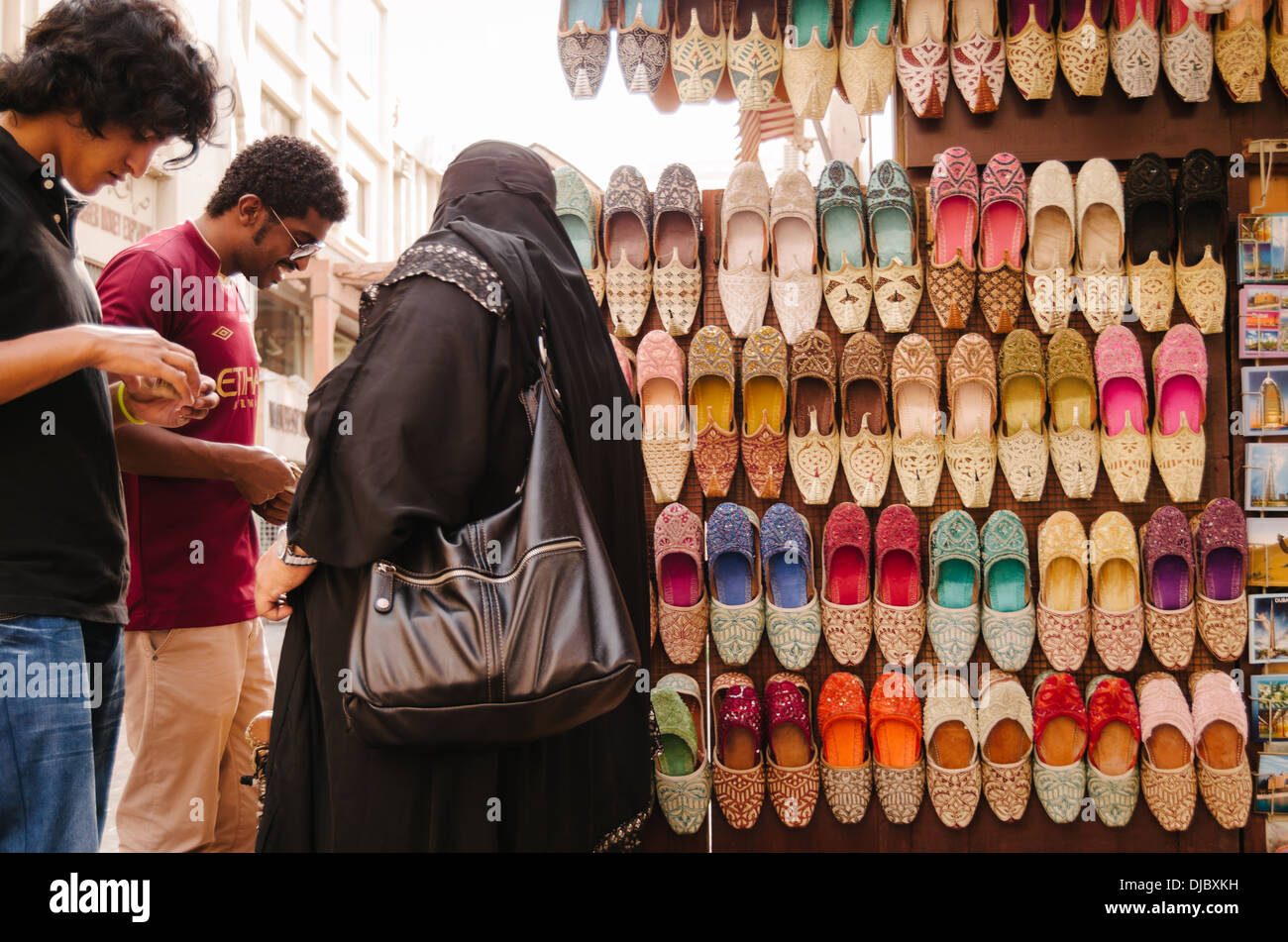 Arab woman wearing a burka haggles with a vendor selling traditional indian shoe at Bur Dubai Souk. Dubai, United Arab Emirates. Stock Photo