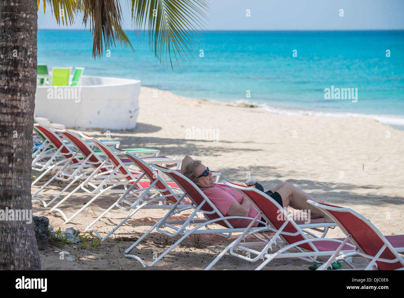 A 78 year old Caucasian woman relaxes in a chaise lounge on the beach in St. Croix, U.S. Virgin Islands. Cottages by the Sea resort. Stock Photo