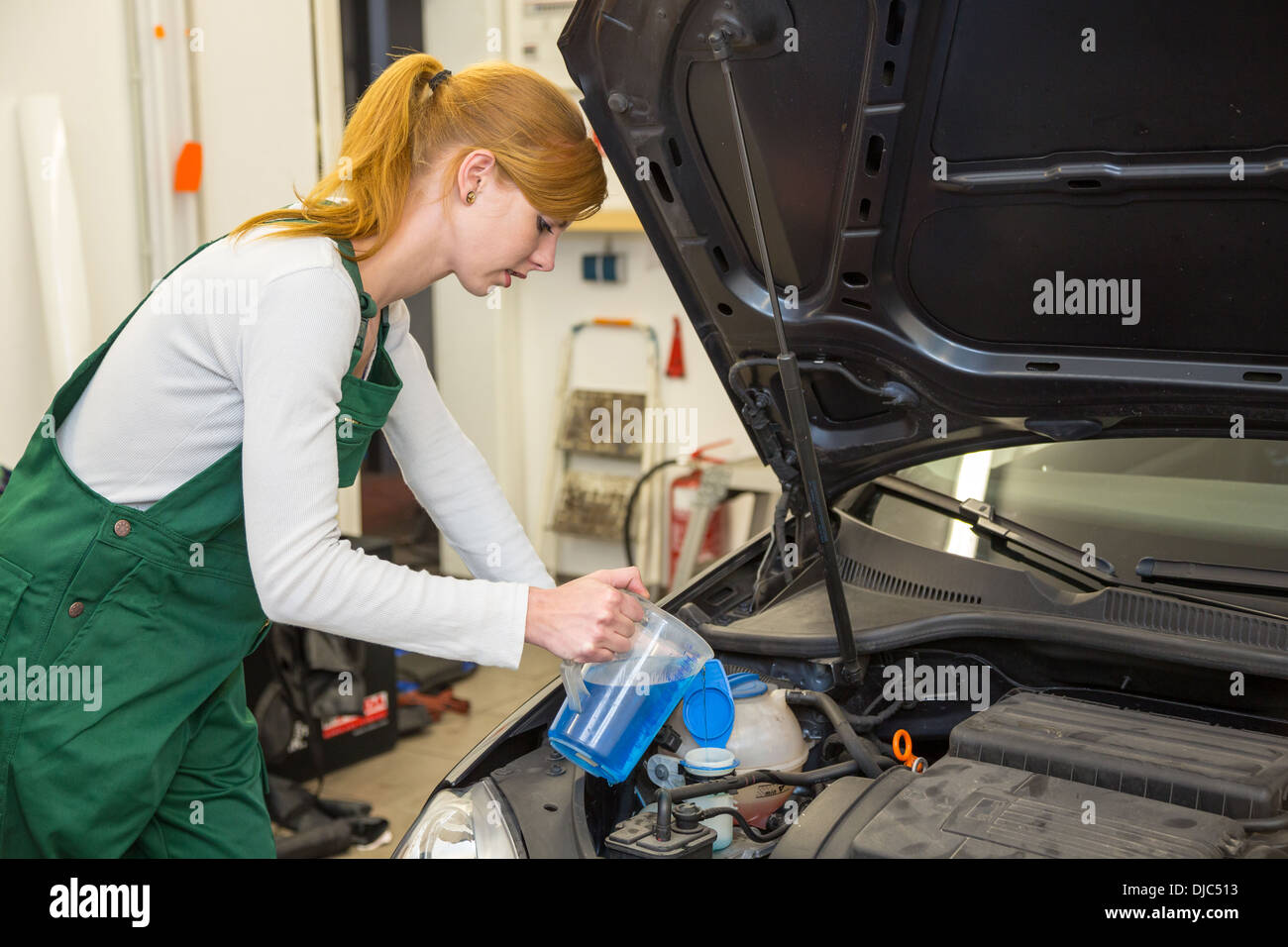 Female mechanic refills coolant or cooling fluid in motor of a car Stock Photo