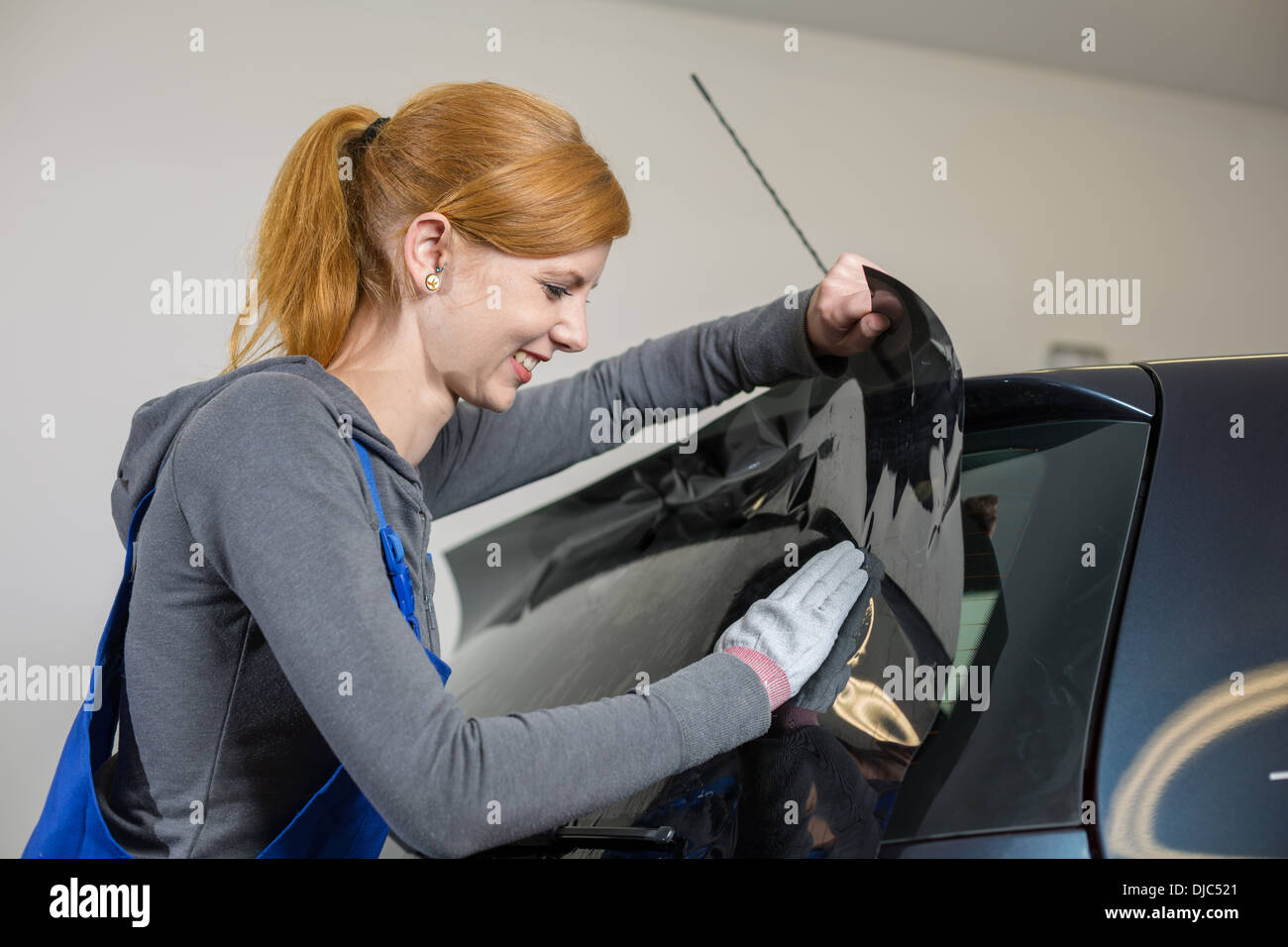 Car wrappers tinting a vehicle window with a tinted foil or film using heat gun and squeegee Stock Photo