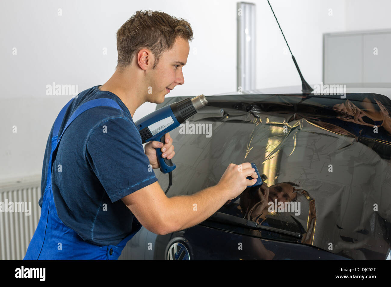 Worker in garage tinting a car window with tinted foil or film Stock Photo