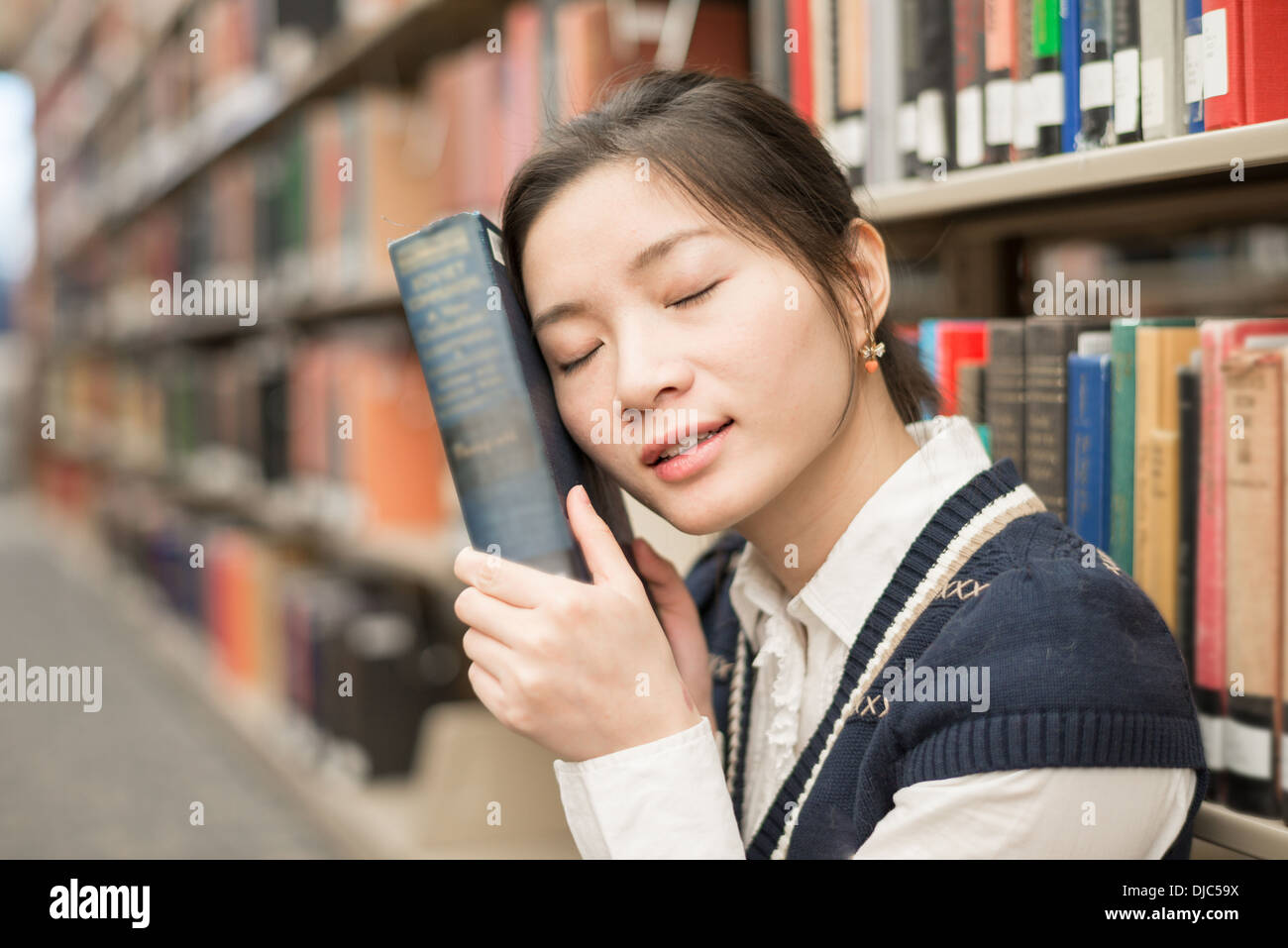 Young girl sitting in front of a bookshelf resting head on a thick old book Stock Photo