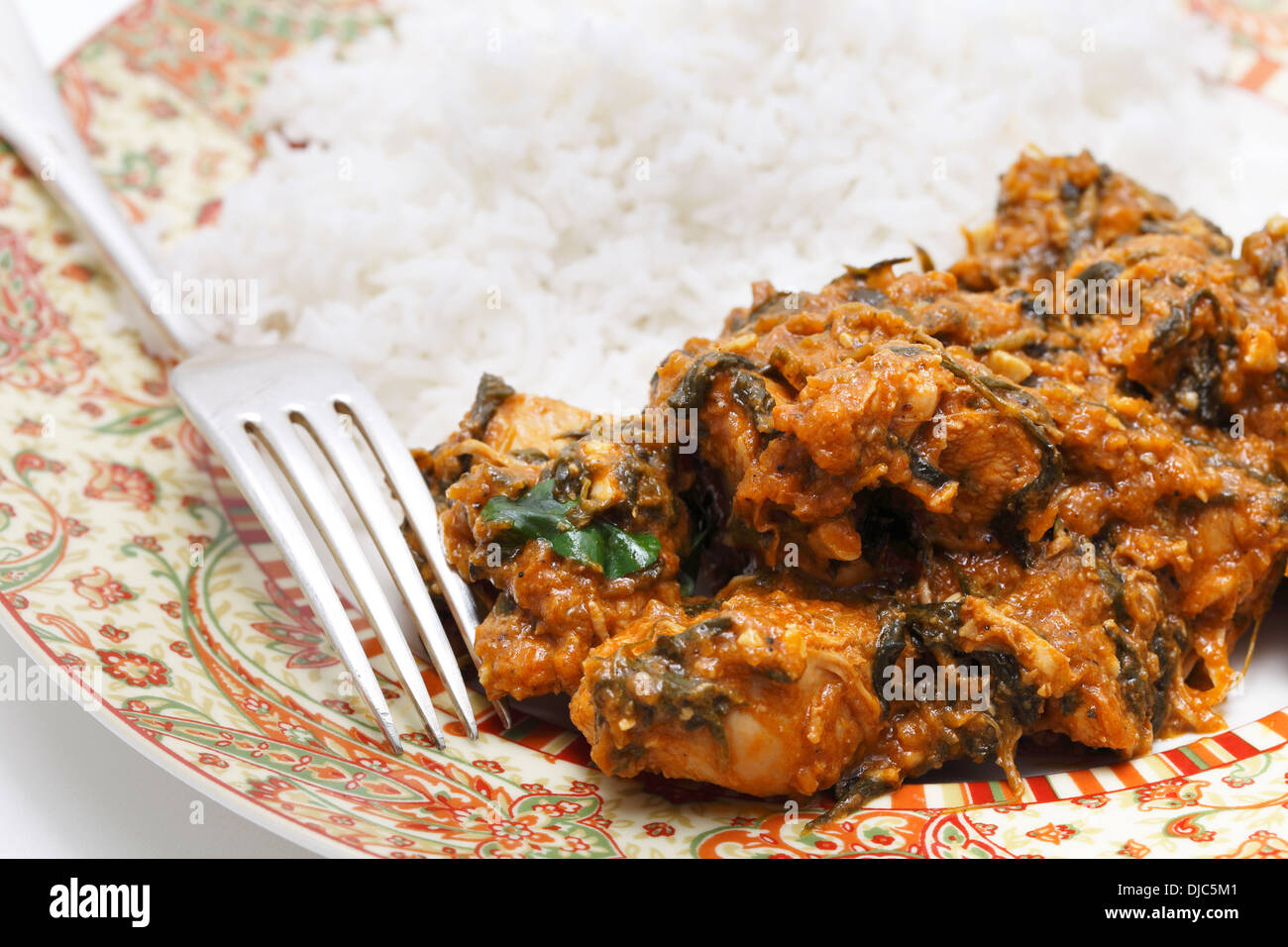 Methi murgh - chicken cooked with fresh fenugreek leaves on a plate with basmati rice and a fork Stock Photo