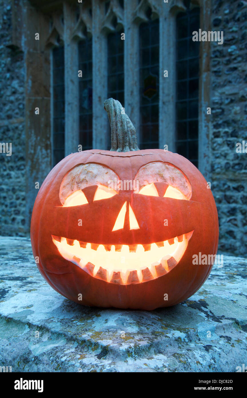 All Hallows Eve. A Halloween Jack o’ Lantern carved from a pumpkin, glowing by candlelight, in an ancient churchyard. England, United Kingdom. Stock Photo