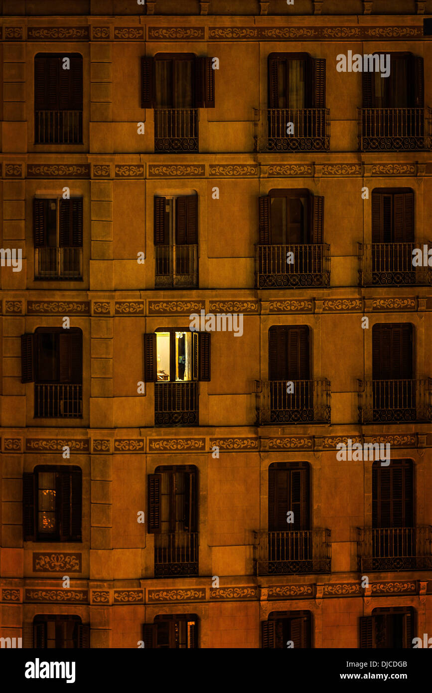 A single apartment light shines through the dark facade of a downtown building. Stock Photo