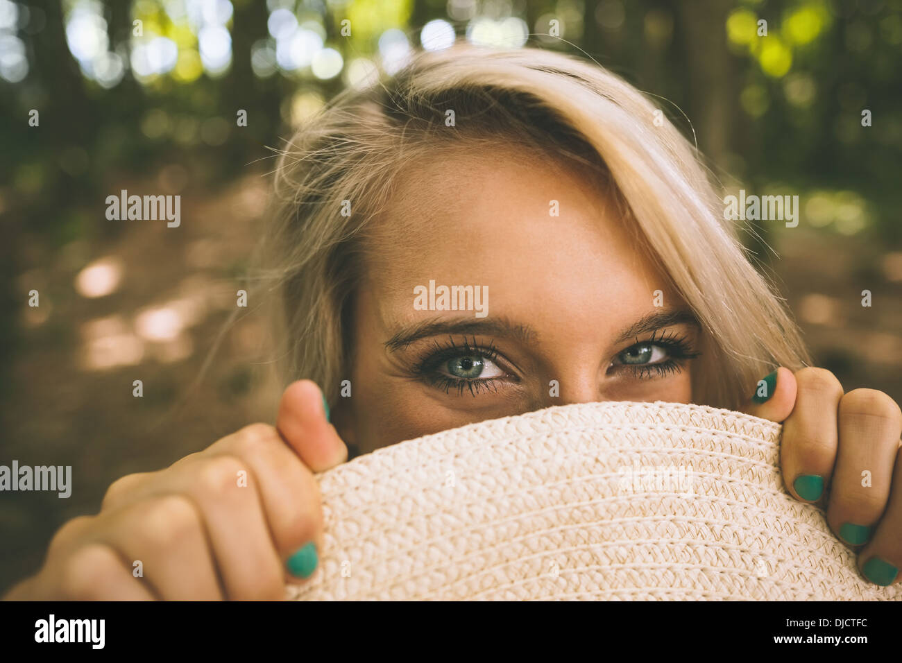 Happy gorgeous blonde holding straw hat in front of her face Stock Photo