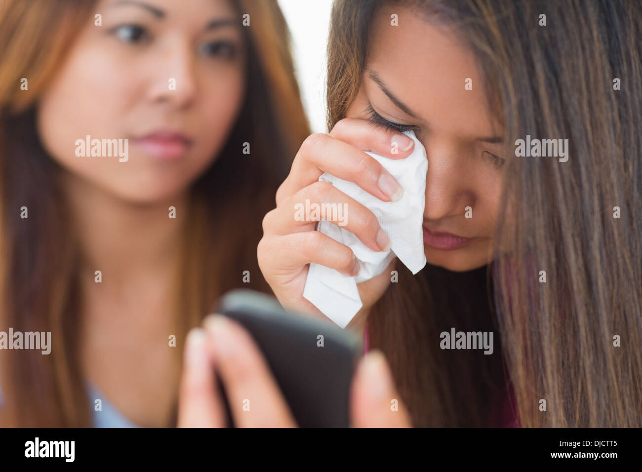 Crying woman looking at phone being comforted by her sister Stock Photo