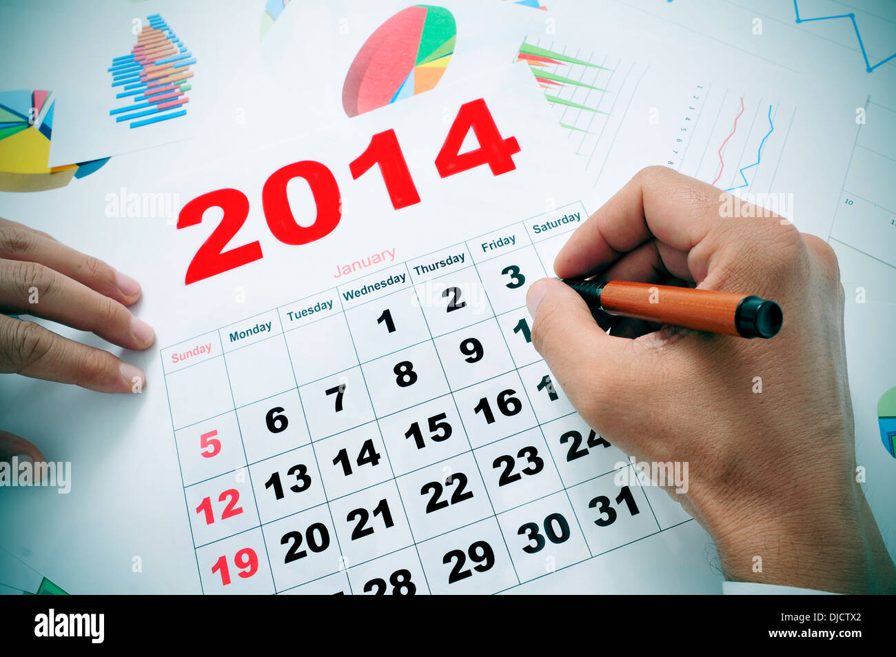 someone at the office taking a look to a 2014 calendar and a pile of charts Stock Photo