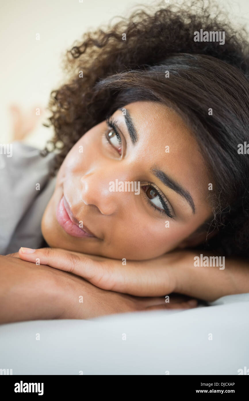 Pretty day dreaming brunette resting head on hand lying on bed Stock Photo