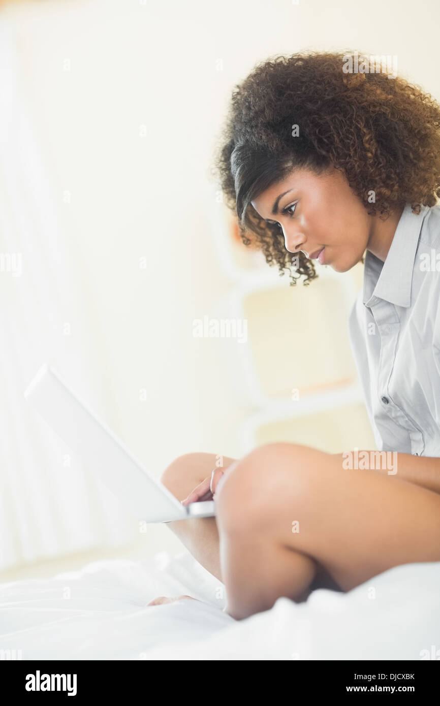 Pretty focused brunette sitting on bed using laptop Stock Photo