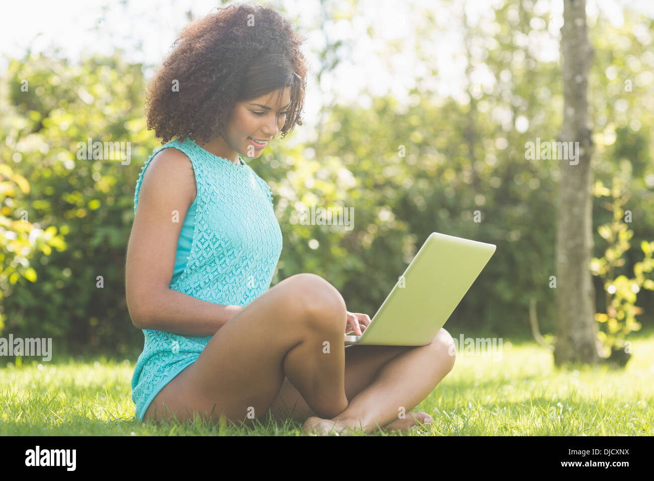 Gorgeous pleased brunette sitting cross legged on grass using laptop Stock Photo