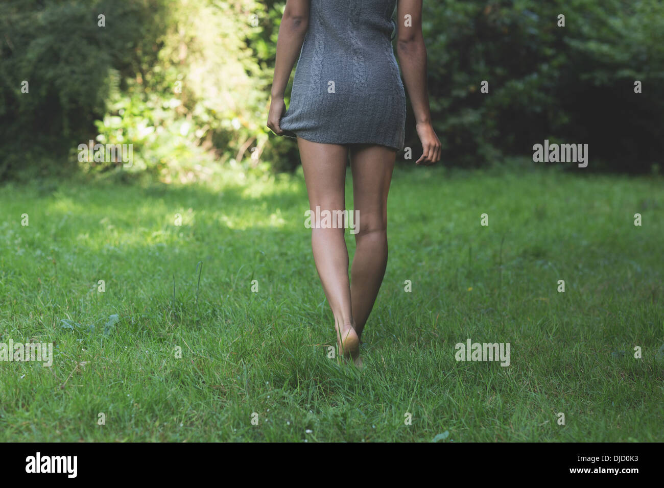 Rear view of lower body of model walking on grass holding dress Stock Photo