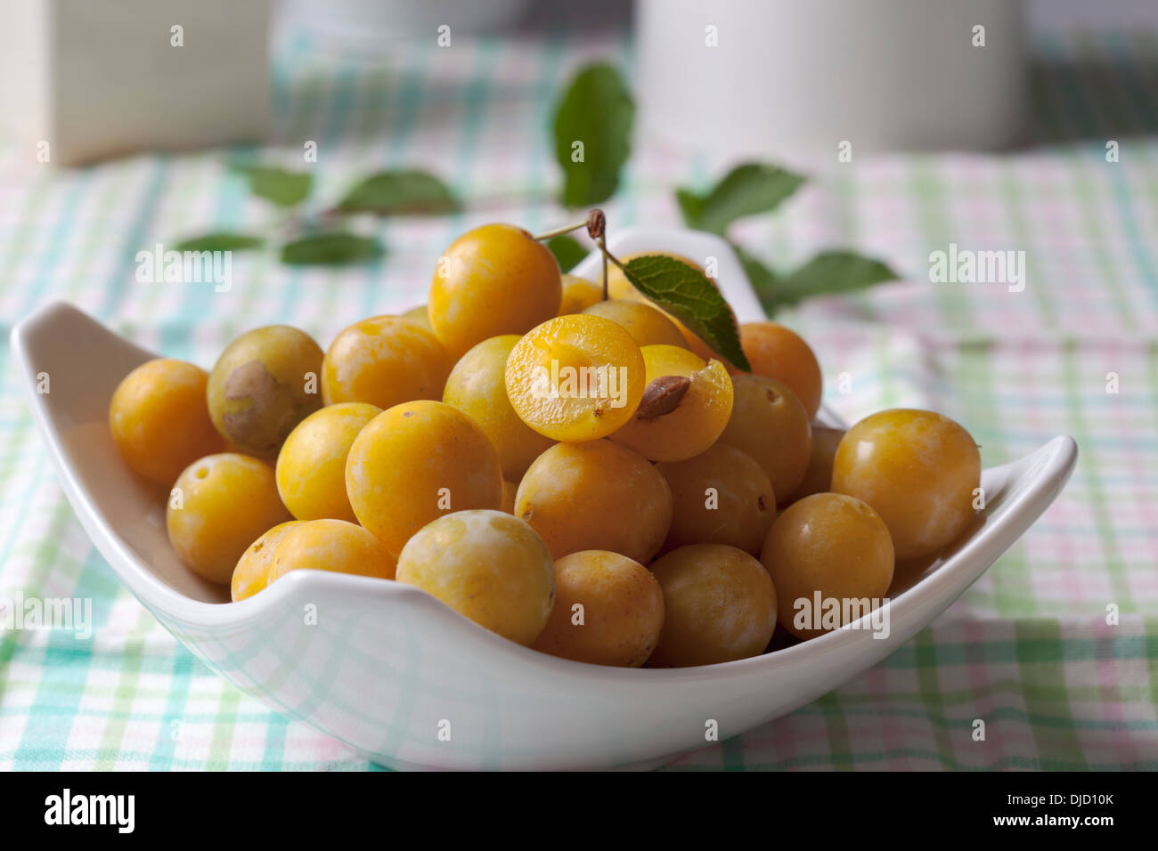 Mirabelles (Prunus domestica subsp. syriaca) in a bowl on wooden table, studio shot Stock Photo