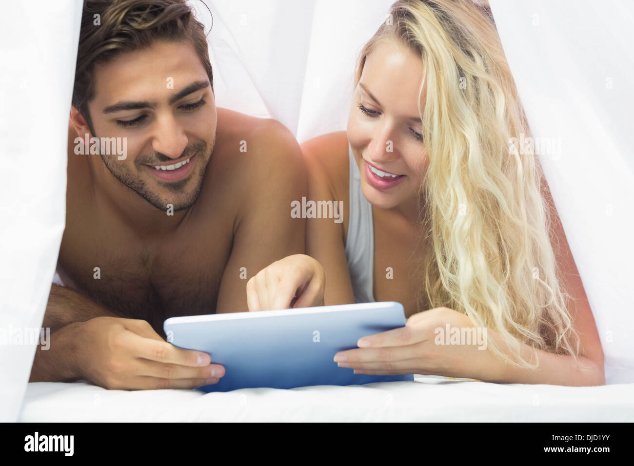 Cheerful couple lying under the sheet using a tablet Stock Photo