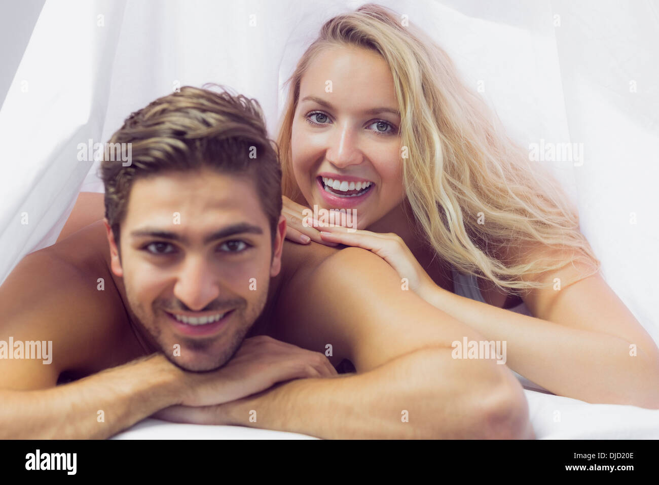 Smiling young couple lying under a blanket Stock Photo