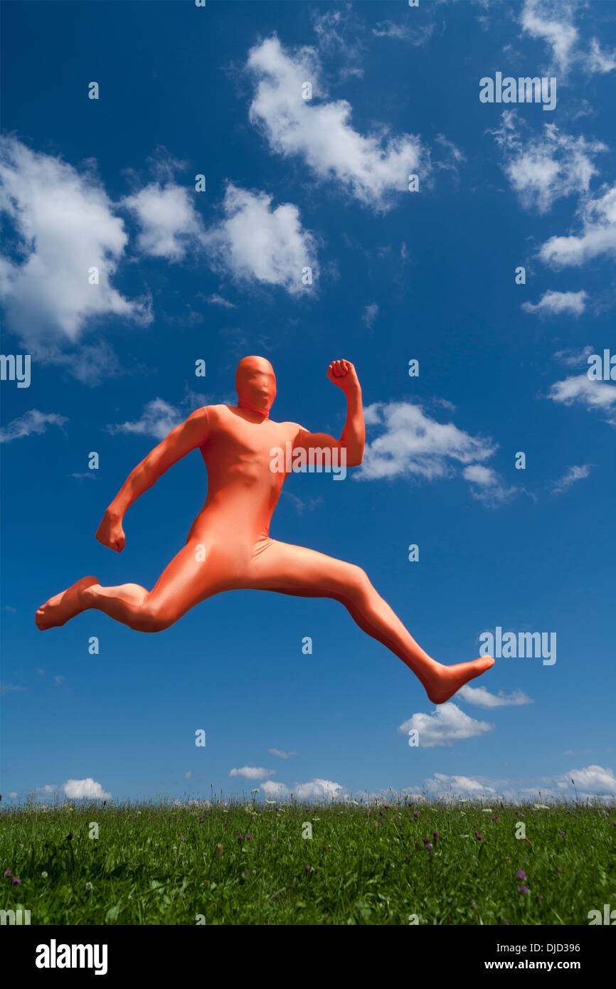 Germany, Bavaria, Man in orange zentai jumping in landscape Stock Photo