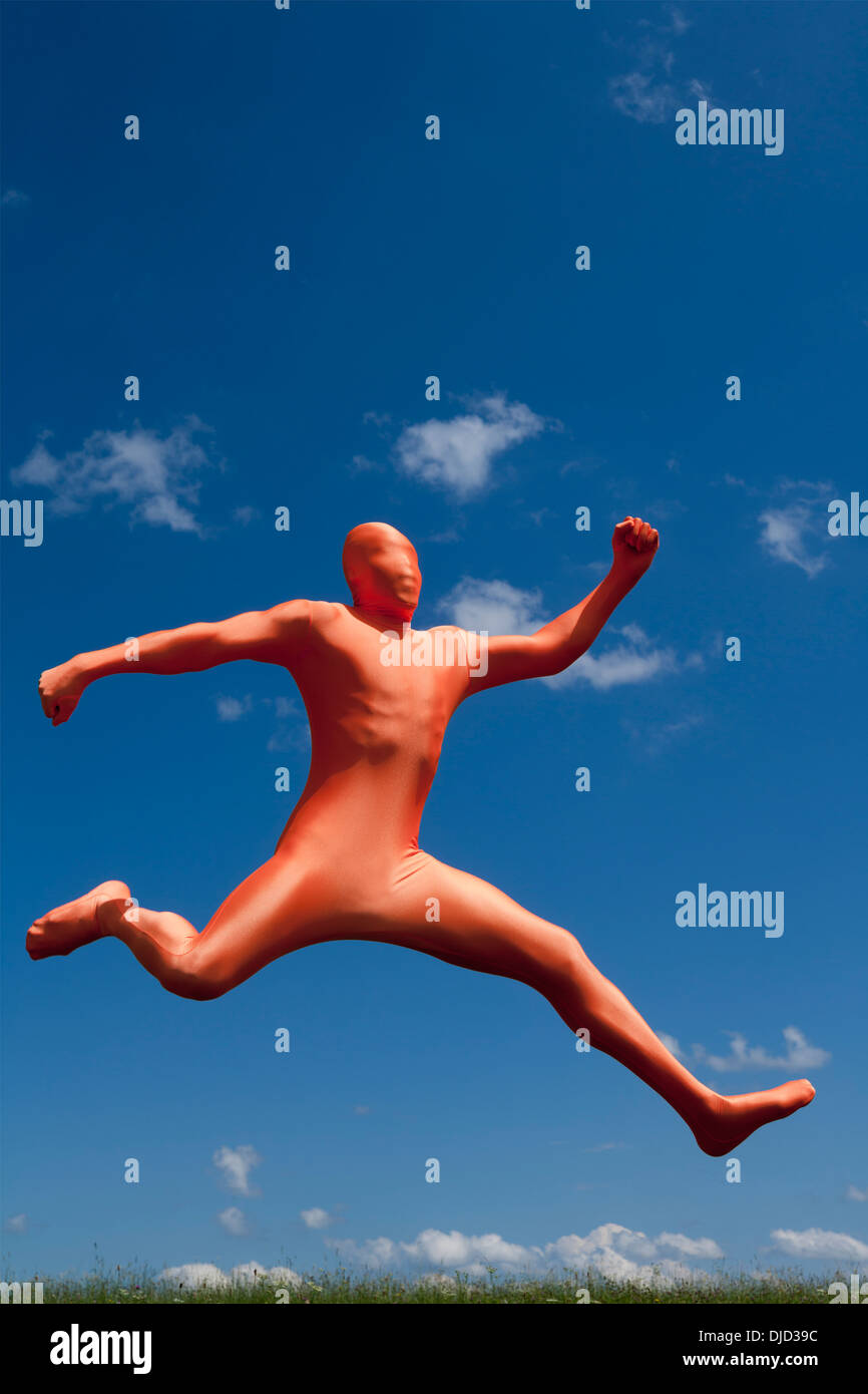 Germany, Bavaria, Man in orange zentai jumping in landscape Stock Photo