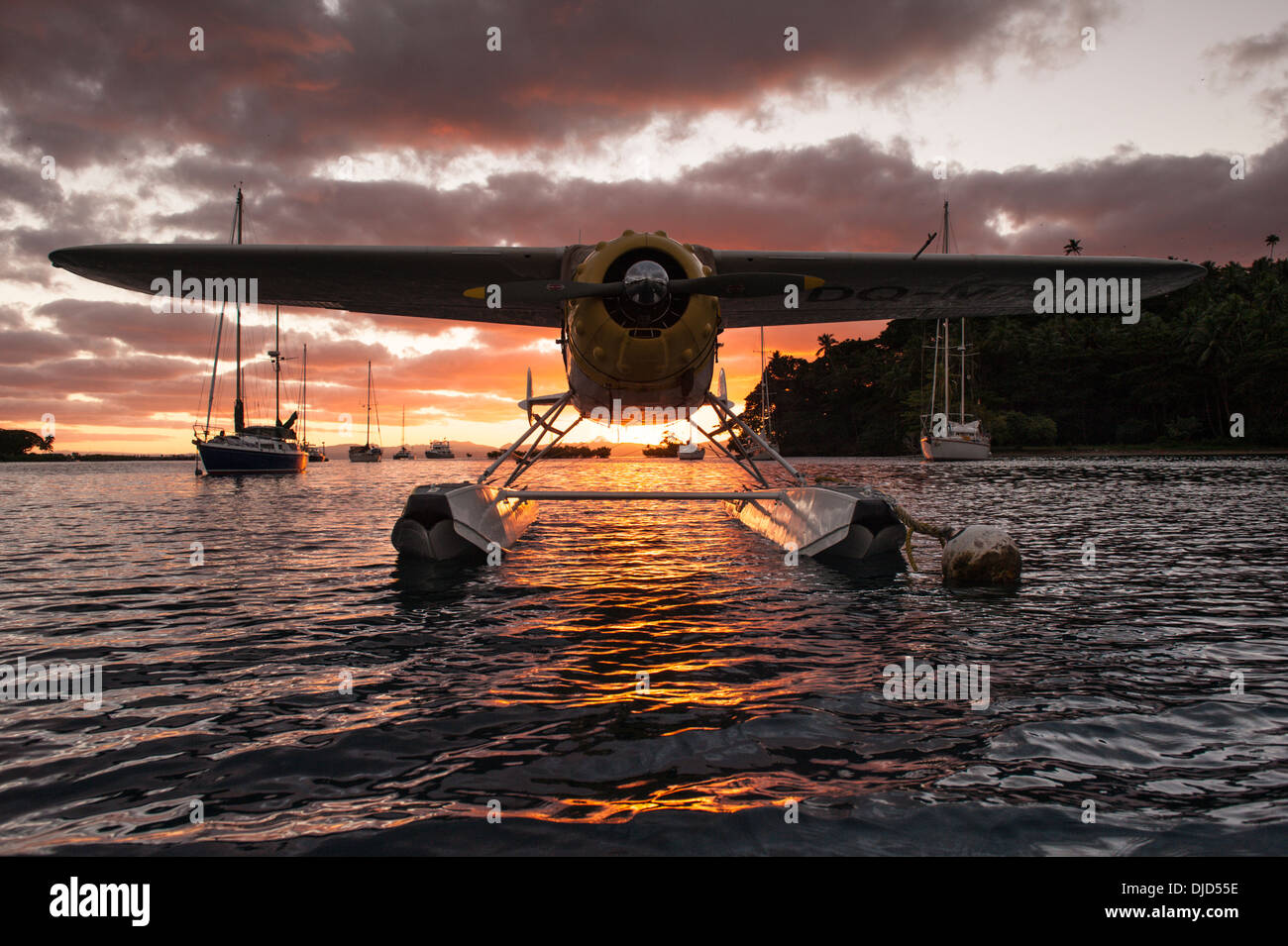 A privately owned seaplane tied to a Copra Shed Marina buoy in front of yachts moored on other buoys at sunset. Savusavu, Fiji Stock Photo