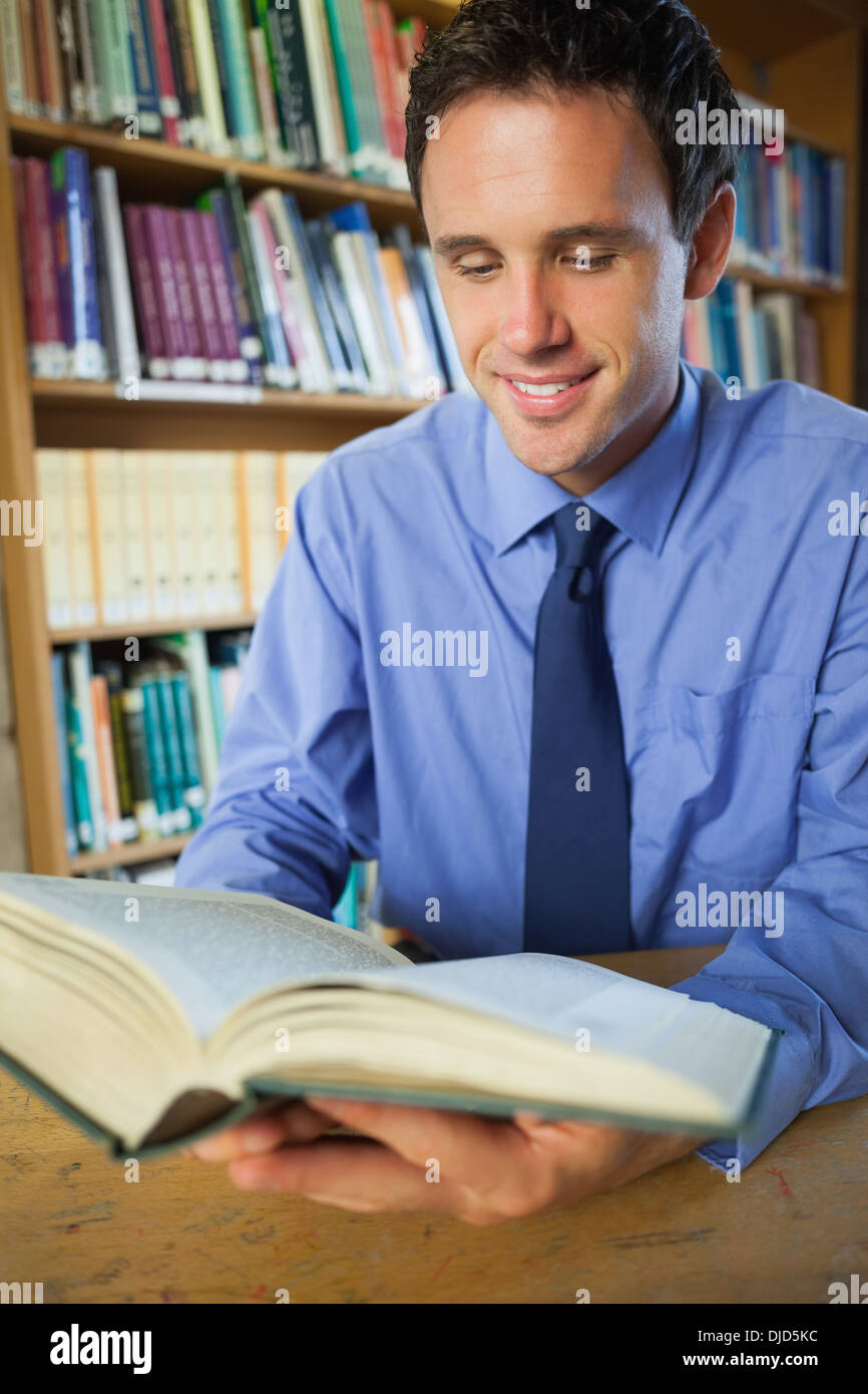 Happy librarian sitting at desk reading a book Stock Photo