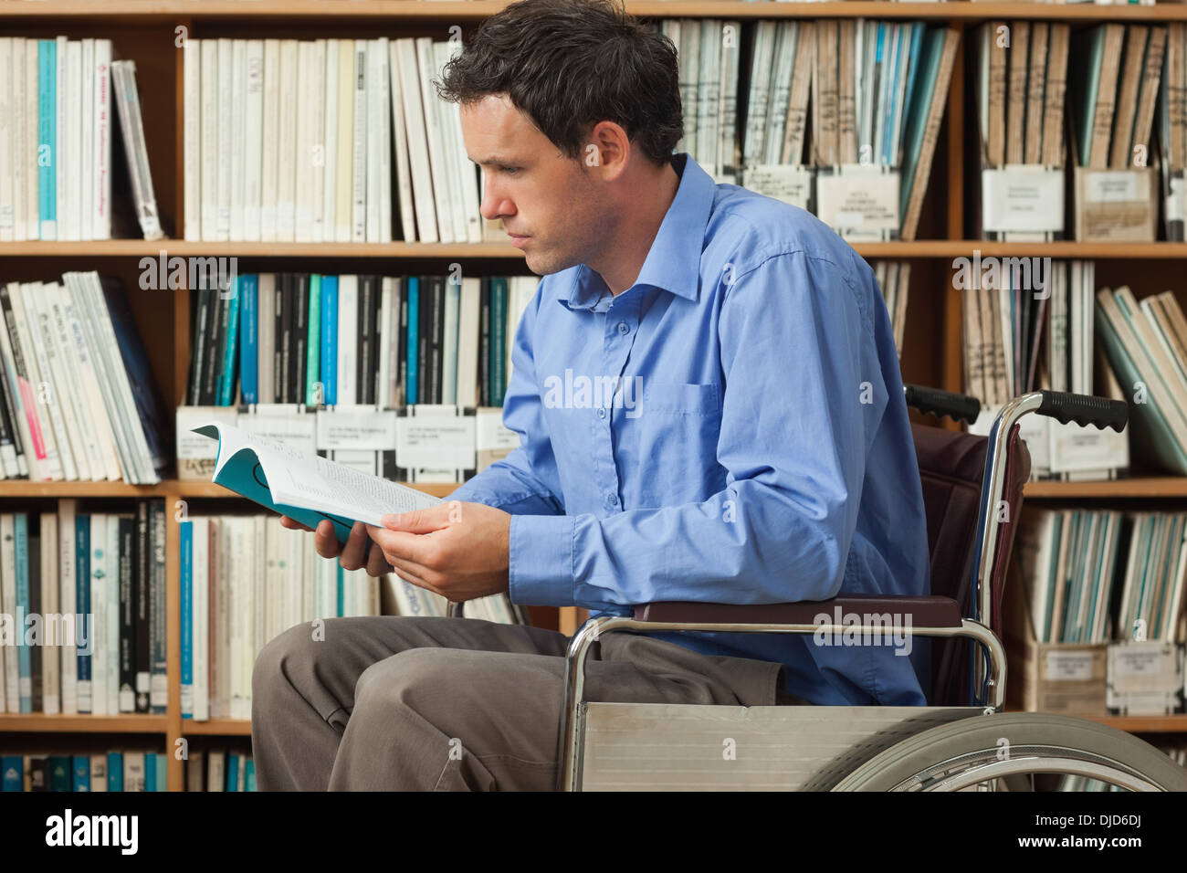 Serious man sitting in wheelchair reading a book Stock Photo