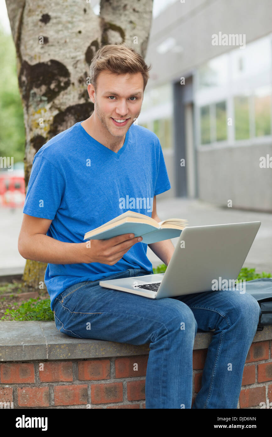 Smiling handsome student sitting on wall studying Stock Photo